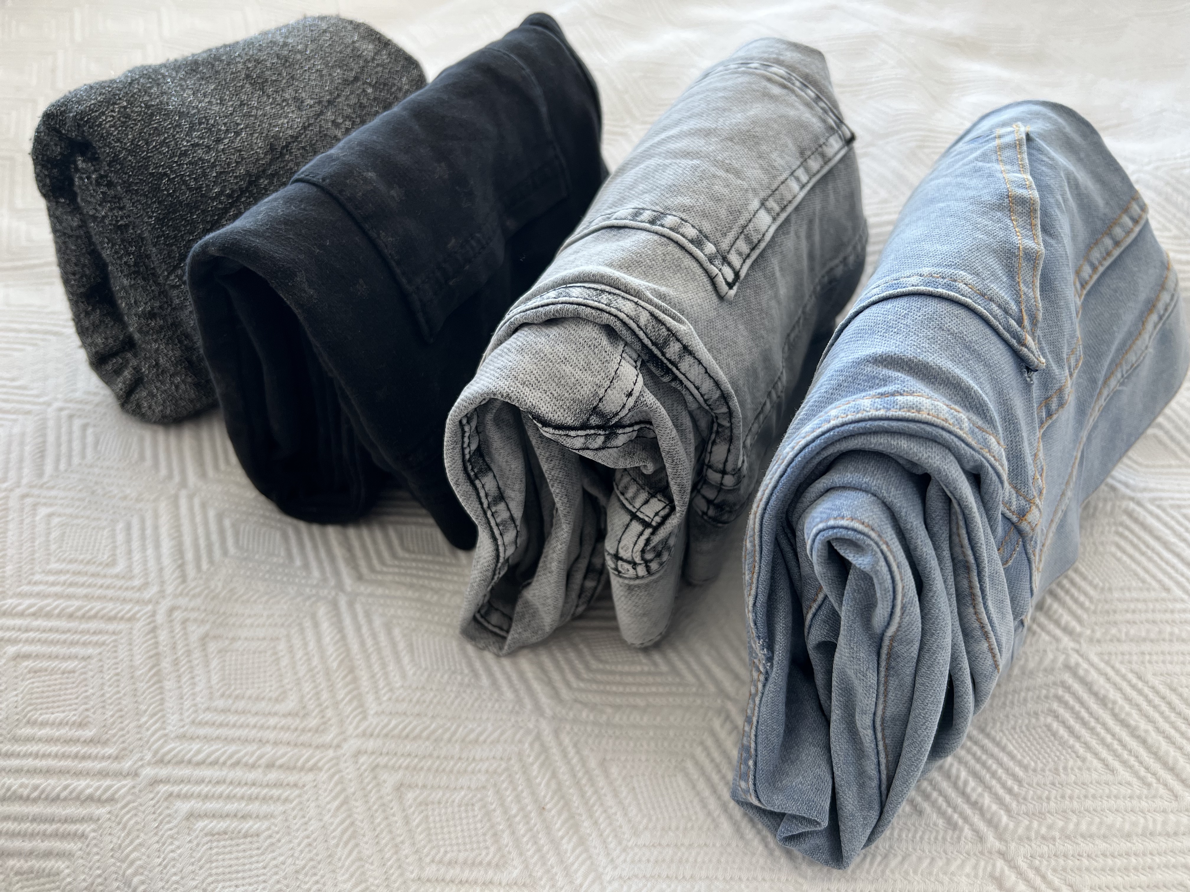 Folded clothes standing on end on a white bedspread