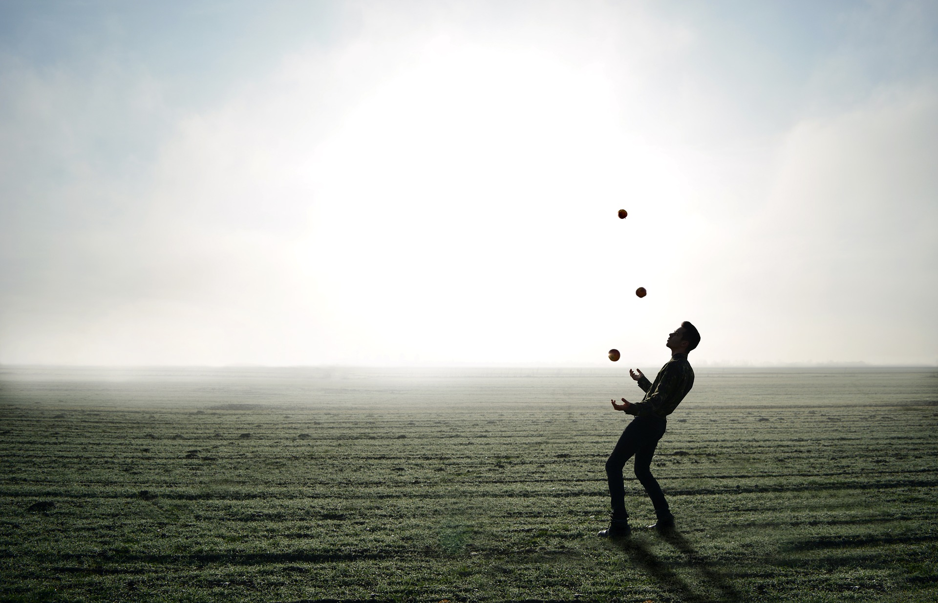 A juggler with three balls on a misty and empty field
