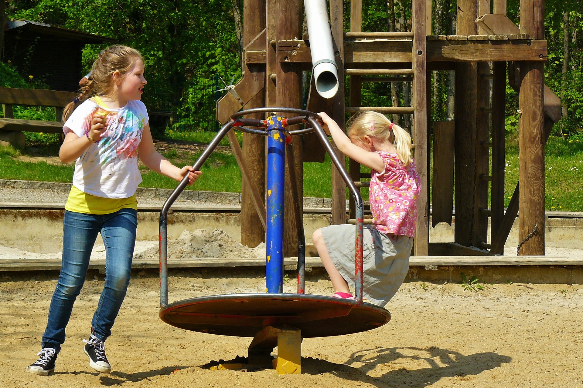 Two kids playing with a carousel at a playground.