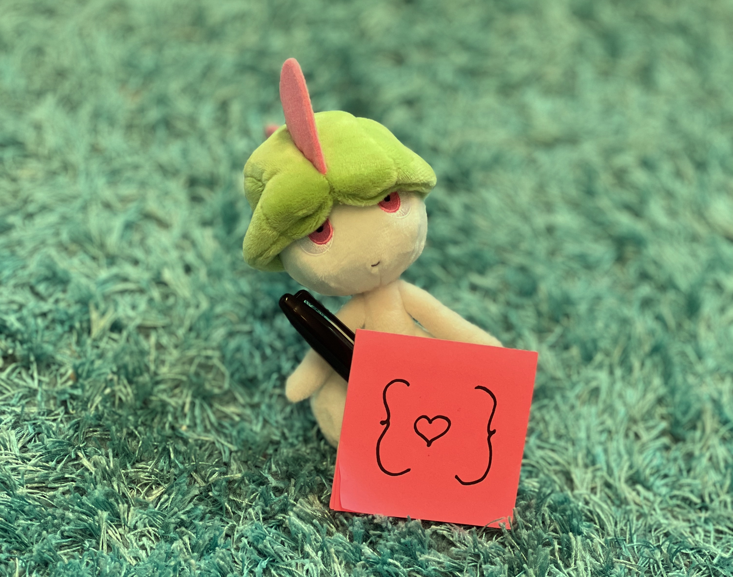 A plushy of the pokémon Ralts, holding sticky notes with 