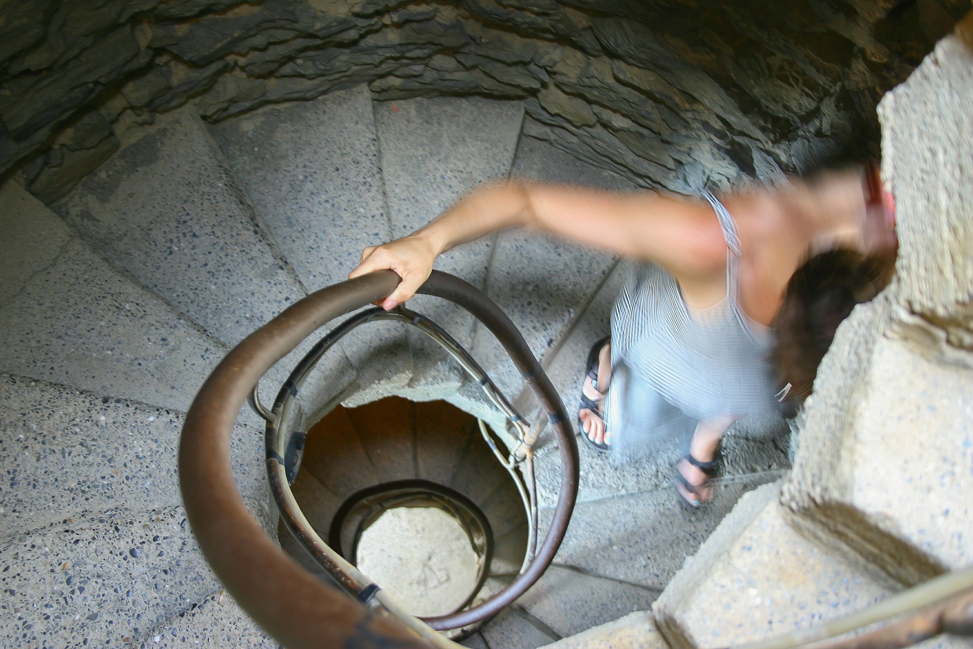 A person gripping the hand rail while running down a spiral staircase.
