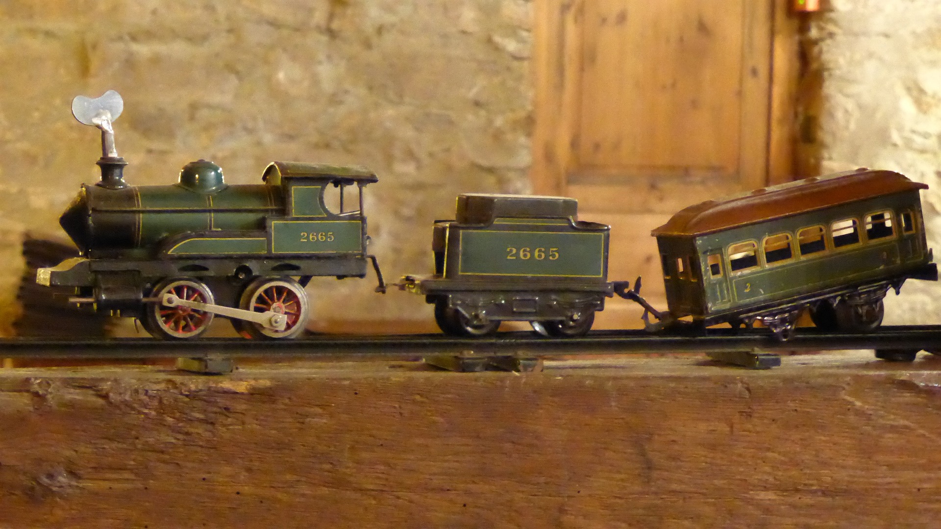 An antique toy train with two carriages, that almost stays on the track.